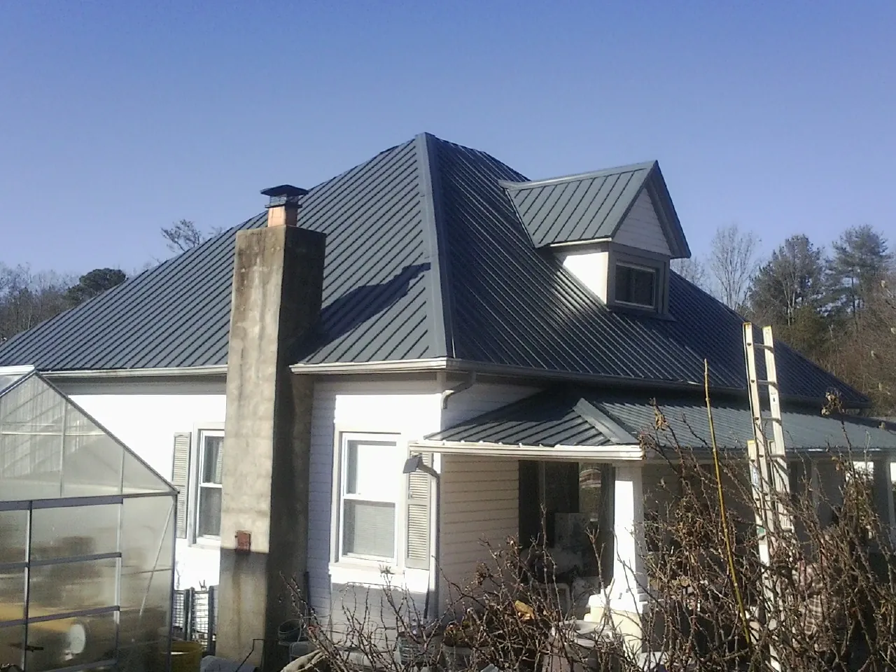 Dark blue standing seam metal roof on a white farmhouse with dormer — Slate & Tile Roof Repair by Roofing Brothers in Latham