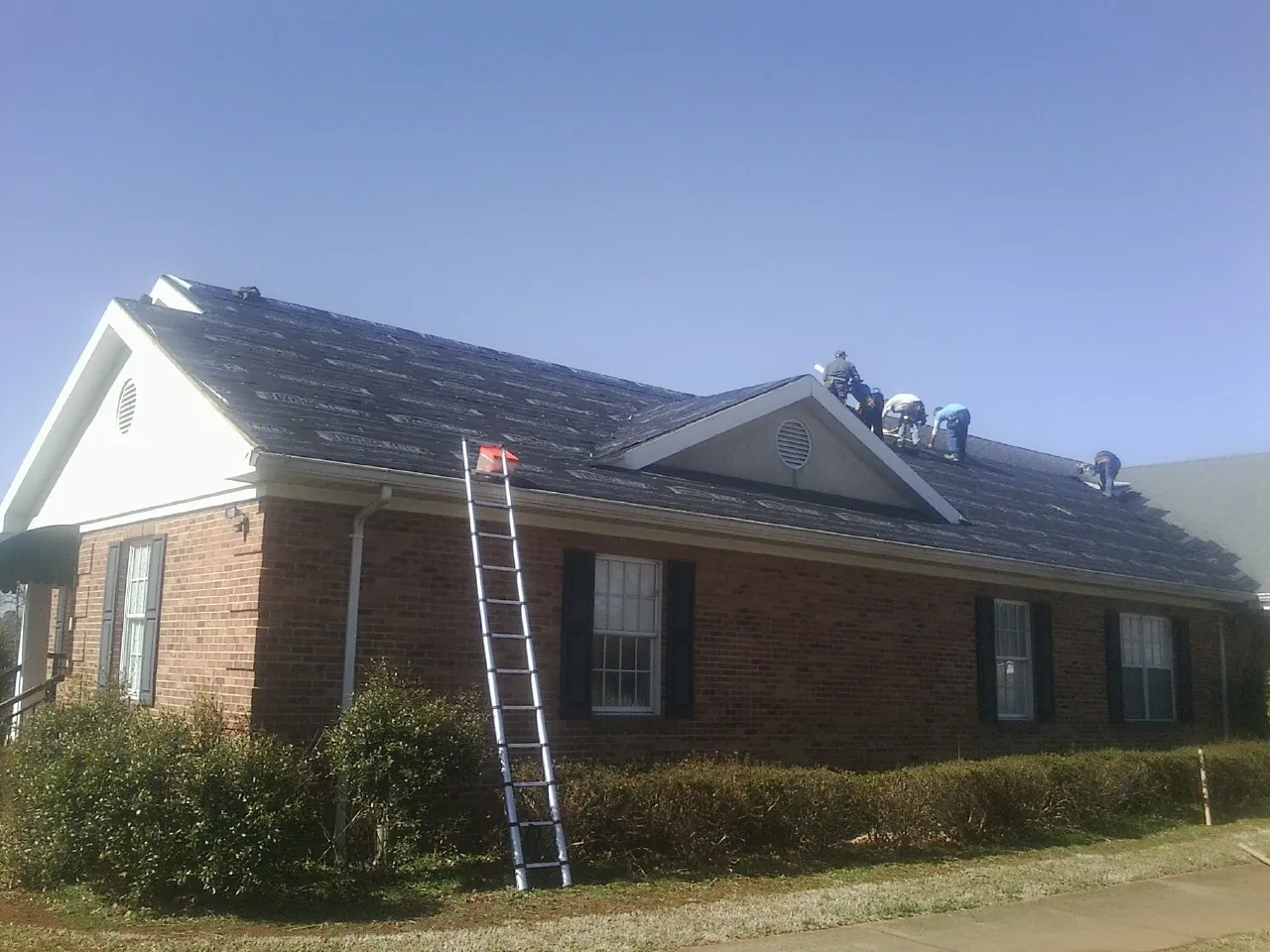 Crew tearing shingles off a brick ranch roof with a ladder set — Emergency Roof Repair work by our crew in Latham