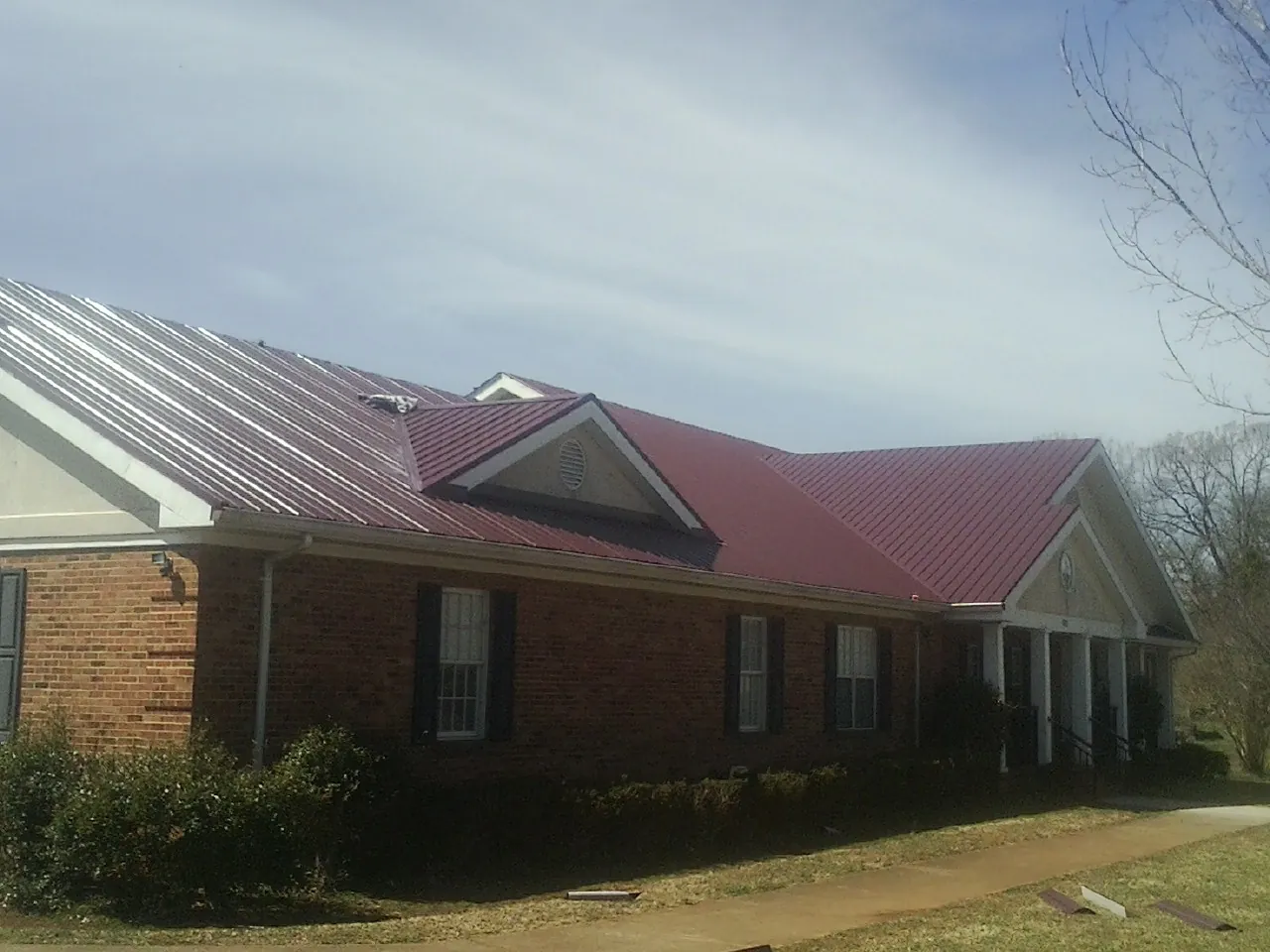 Red metal roof with gabled entries on a long brick building, from a Hail Damage Roof Repair job in Latham