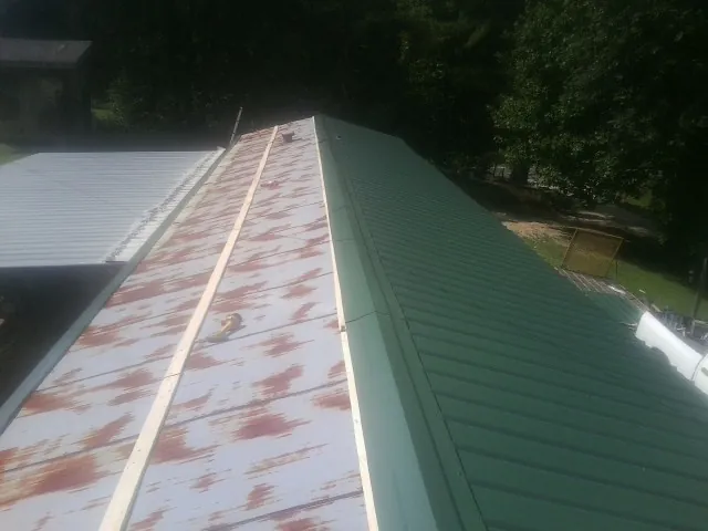 Old rusted panels beside newly installed green metal roofing — Wind Damage Roof Repair by Roofing Brothers in Latham