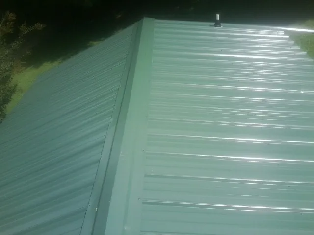 New green metal panels meeting at the ridge of a roof — Flat Roof Repair work by our crew in Latham