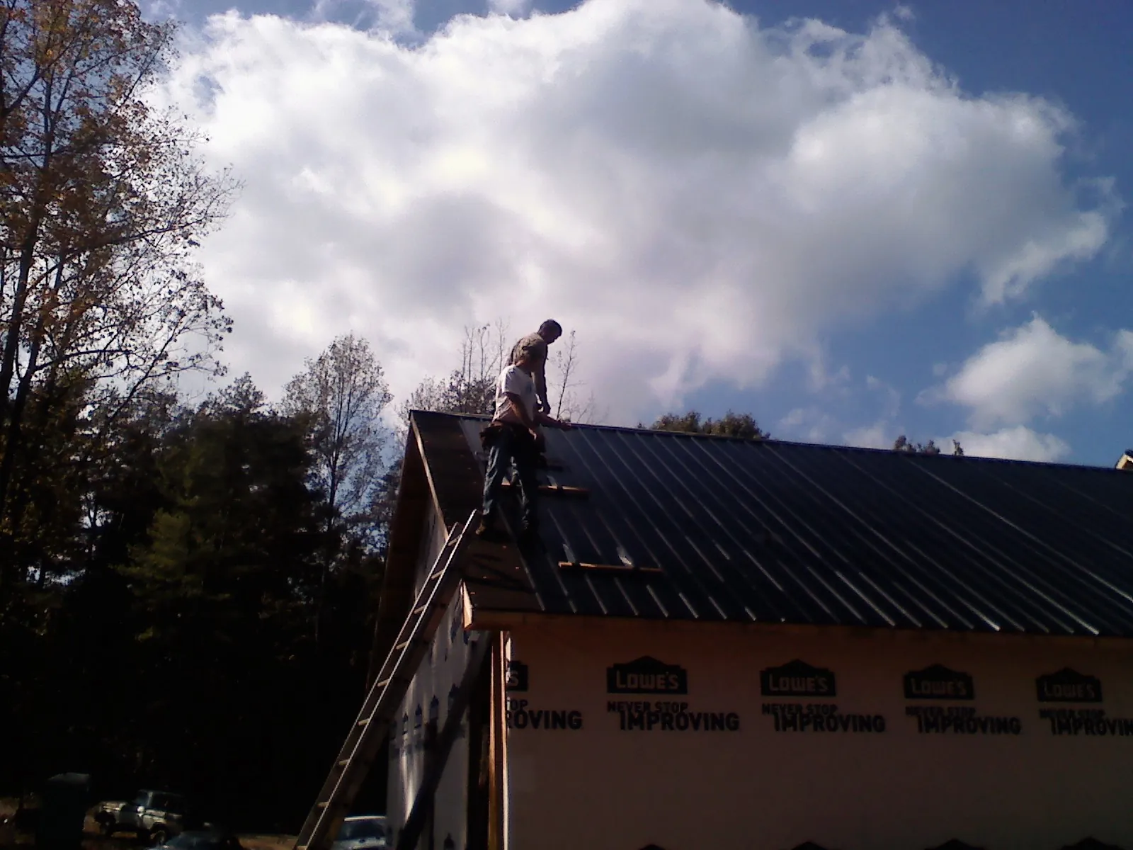 Roofer fastening dark metal panels high against a cloudy sky, from a Roof Inspection job in Latham