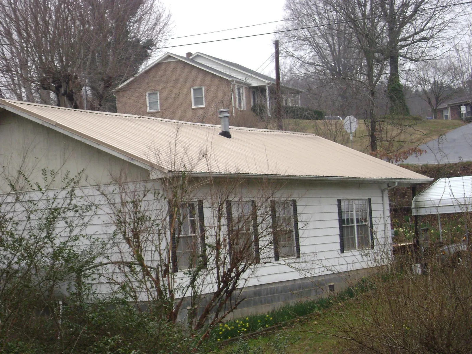 Tan metal roof on a white sided house set into a hillside — Commercial Roofing by Roofing Brothers in Latham