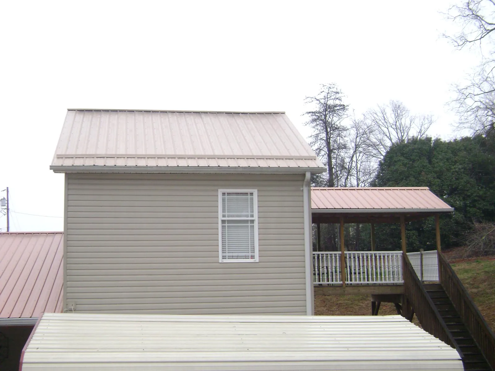 Tan metal roofs on a two story addition and attached porch, from a Roof Replacement job in Latham